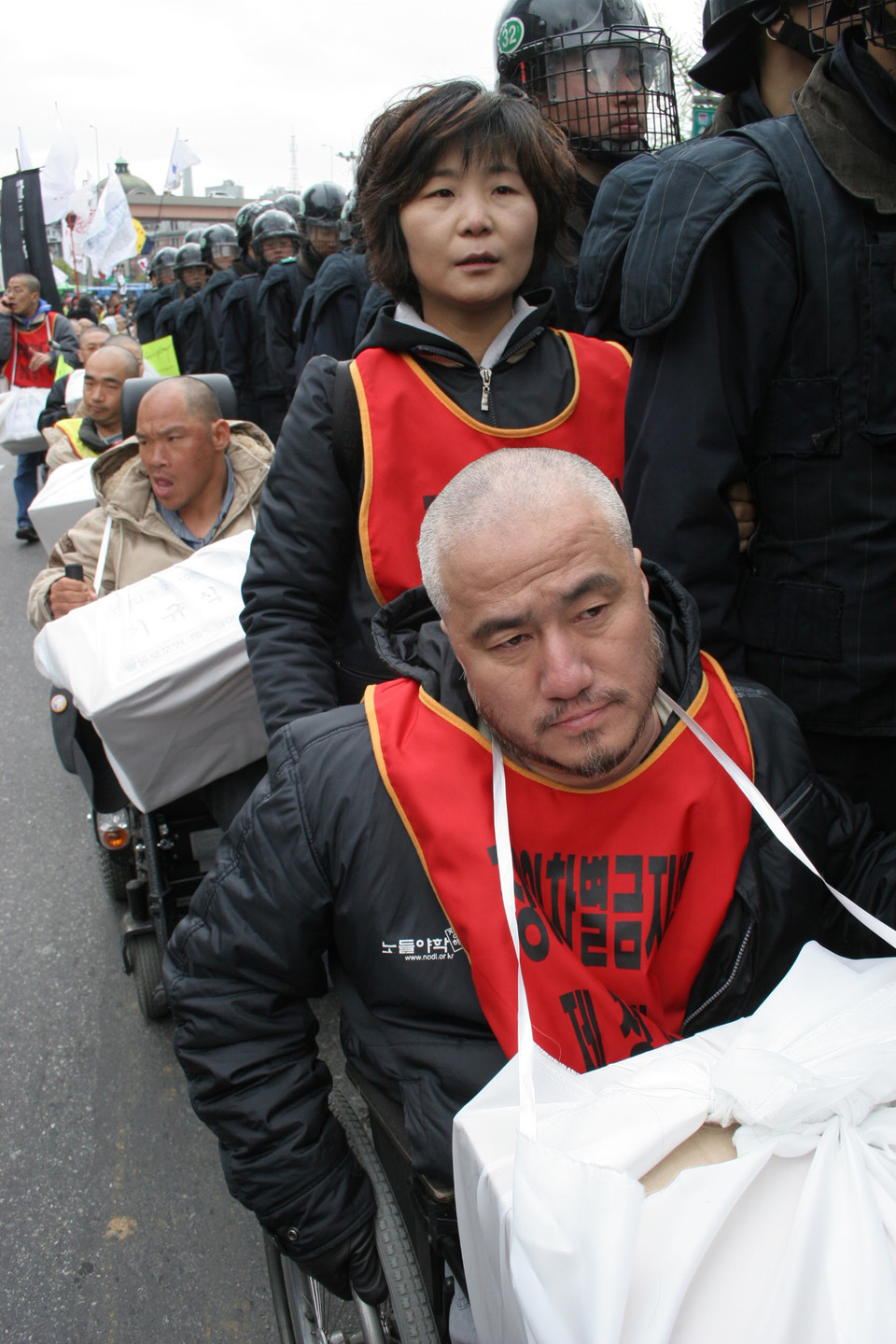 2006년 활동보조제도화를 요구하며 삭발한 박경석 전장연 대표가 잘린 머리카락을 들고 행진하고 있다. 그의 휠체어를 뒤에서 박옥순 활동가가 밀고 있다. 사진 전진호 