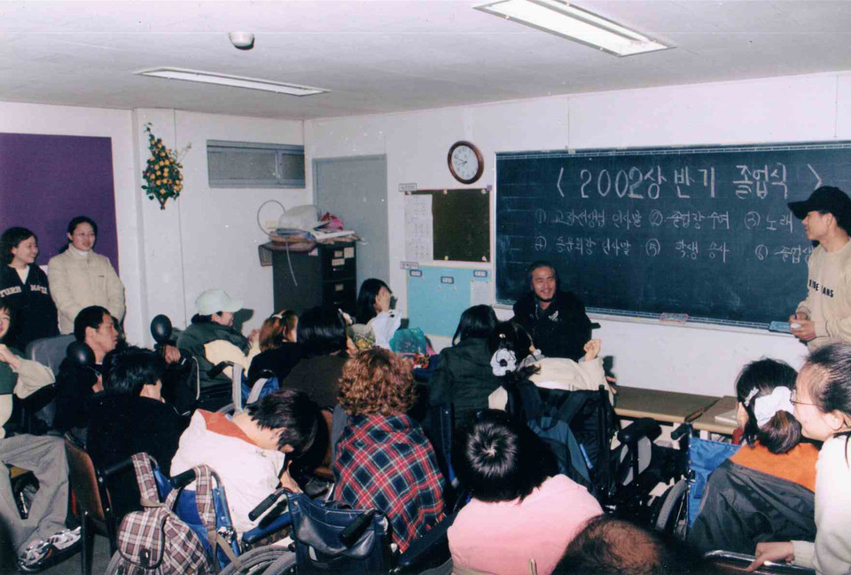 2002년 8월, 노들야학 상반기 졸업식이 열리고 있다. 사진 왼쪽 서 있는 사람(검은색에 영어 쓰여 있는 옷)이 이진희 활동가다. 사진 제공 노들야학 