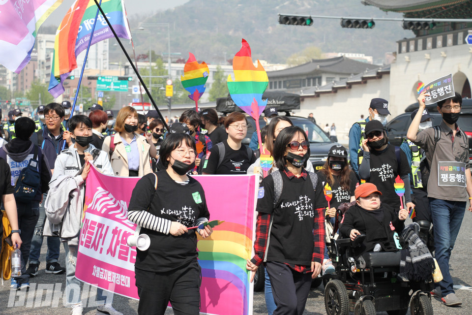 2018년 4월 20일 ‘장애인차별철폐의 날’에 장애여성공감 활동가들이 차별금지법 제정을 촉구하는 현수막을 들고 행진하고 있다. 왼쪽 맨 앞에 이진희 활동가가 있고, 오른편에는 전동휠체어를 탄 조미경 활동가가 무지개 모양의 모형 횃불을 들고 행진하고 있다. 사진 강혜민 