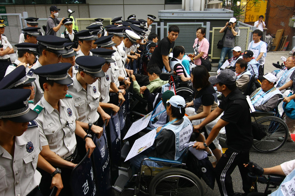 2009년 6월 17일, 자립생활을 원하는 중증장애인 100명은 서울 혜화동 로터리에서 탈시설 자립생활 권리 쟁취 100인 선언 기자회견을 열었다. 기자회견을 마친 사람들은 당시 오세훈 서울시장 공관에 공개서한을 전달하려고 했으나 경찰 방패에 길이 가로막혔다. 뒤에 분홍색 티를 입은 사람이 김정하 활동가. 사진 전진호 