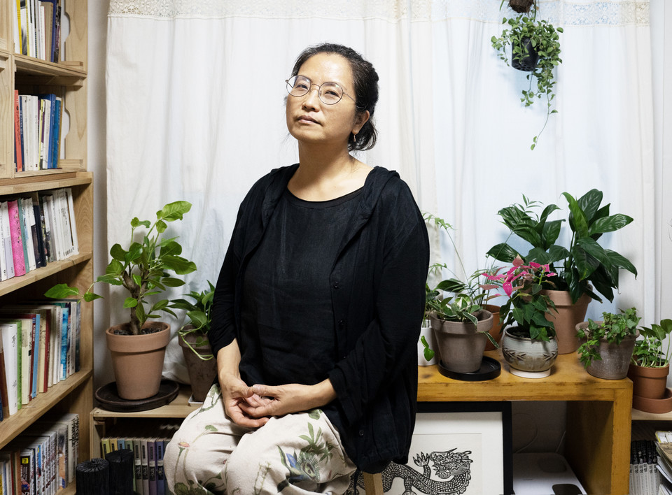 임소연 활동가가 그의 집에서 포즈를 취하고 있다. 그의 뒤로는 초록 식물이 가득하고, 왼쪽 책꽂이에는 책이 꽂혀 있다. 사진 현다혜 