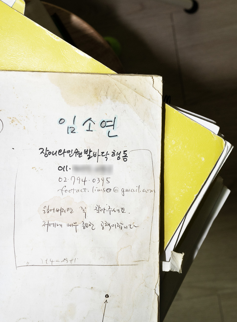 임소연 활동가가 과거 사용했던 노트. 오래된 노트는 누렇게 색이 바라고 얼룩져 있다. 공책에는 “임소연 장애와인권발바닥행동”이라는 글자와 함께 개인 휴대폰, 사무실 전화번호, 이메일 주소가 적혀 있고, 그 아래에는 “잃어버리면 꼭 찾아주세요. 저에게 매우 중요한 공책이랍니다”라는 글자가 쓰여 있다. 사진 현다혜 