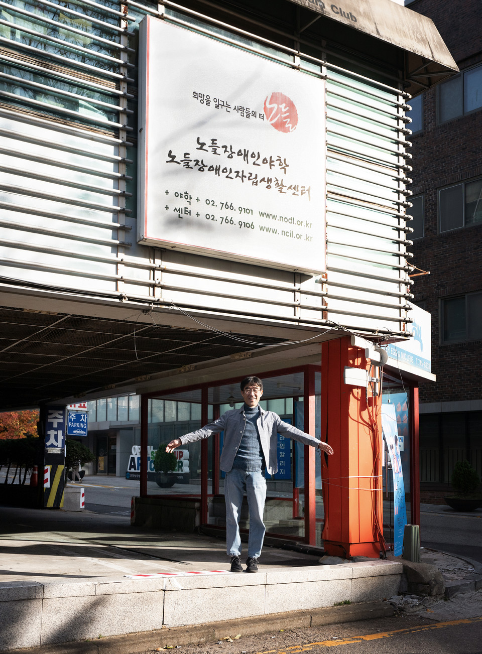 김도현 활동가가 노들장애인야학, 노들장애인자립생활센터가 적힌 큰 간판 아래 환하게 웃으며 서 있다. 사진 현다혜 