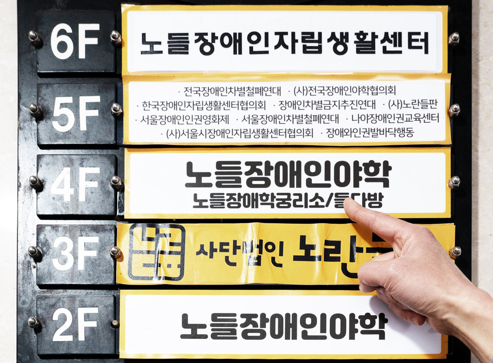 건물 층별 안내도. 노들장애인자립생활센터, 노들장애인야학, 노들장애학궁리소, 사단법인 노란들판, 전국장애인차별철폐연대 등이 적혀 있다. 김도현 활동가가 노들장애인야학과 노들장애학궁리소를 손가락으로 가리키고 있다. 사진 현다혜 