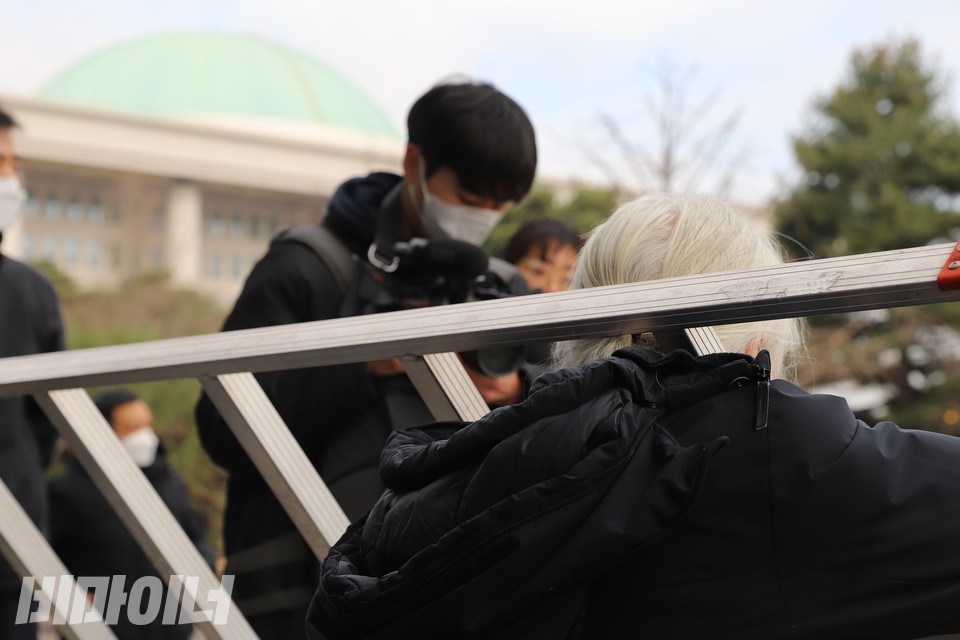사다리를 목에 건 박경석 전장연 상임공동대표 앞으로 국회의사당 지붕이 보인다. 사진 하민지