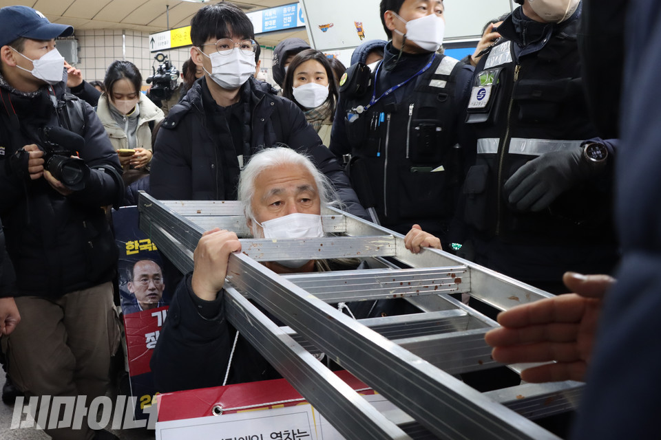 박경석 전국장애인차별철폐연대 상임공동대표가 철제 사다리를 목에 걸고 오전 8시 56분께 삼각지역 숙대입구역 방면으로 들어오는 지하철을 타려 시도하자, 서울교통공사 관계자들이 승강장 입구에서 사다리 반입을 막고 있다. 사진 복건우