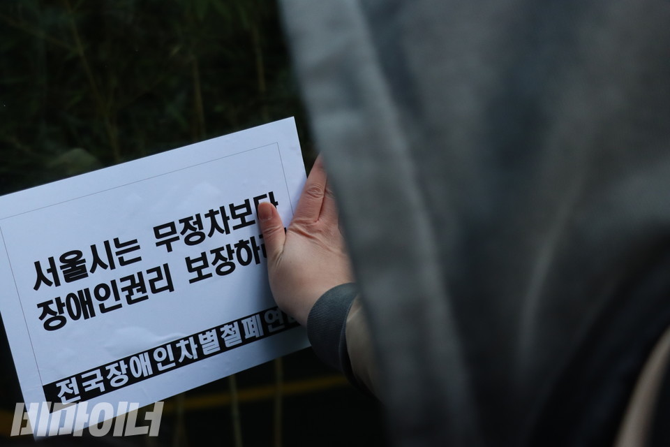 전국장애인차별철폐연대 활동가가 ‘서울시는 무정차보다 장애인 권리 보장하라’고 적힌 스티커를 서울시청 외벽에 붙이고 있다. 사진 복건우