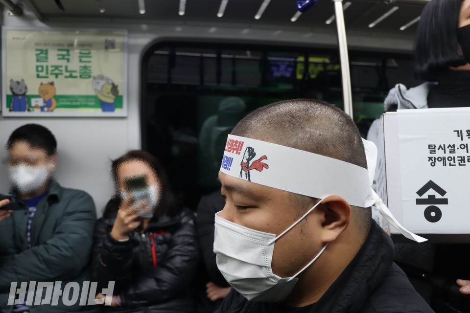 지난달 25일, 송현우 활동가가 삭발 후 지하철 선전전을 진행하고 있다. 건너편에 비장애인 승객들이 좌석에 앉아 있다. 사진 하민지