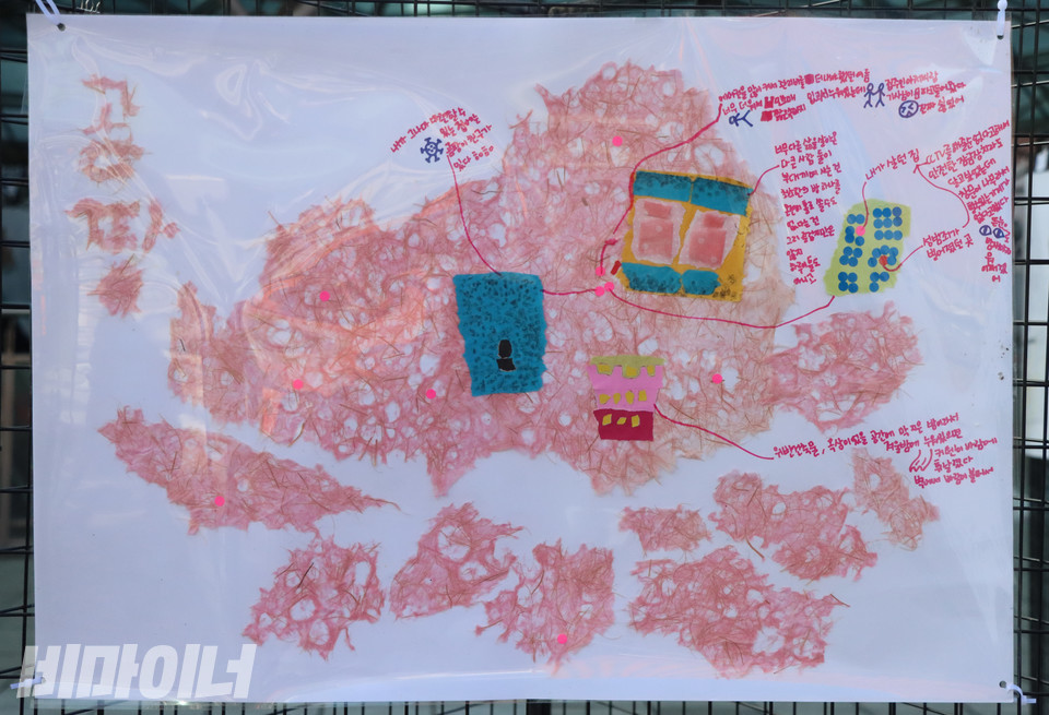 ‘여성홈리스가 나눈 집 이야기’ 전시 중 여성홈리스 당사자 지수(가명) 씨가 그린 심리지도. 곰팡이를 연상시키는 붉은 배경 위에 그가 머물렀던 거처들이 글과 그림으로 묘사되어 있다. ‘내가 그나마 마련할 수 있는 집에는 곰팡이 친구가 있다’, ‘에어컨을 많이 켜서 관리비를 더 내야 했던 여름’ 등이 붉은 글씨로 적혀 있다. 사진 복건우