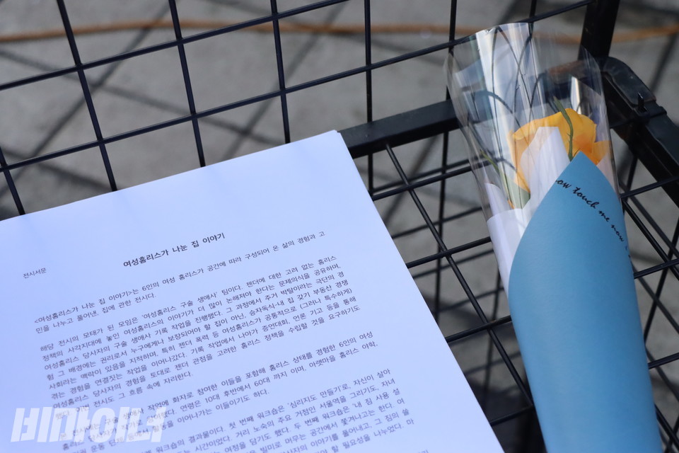 철제 부스 위에 ‘여성홈리스가 나눈 집 이야기’ 전시 서문이 노란 장미와 함께 놓여 있다. 이날 전시회에는 10대부터 60대까지 6명의 여성홈리스가 작가로 참여해 저마다의 홈리스 경험과 고민을 나누고 풀어냈다. 사진 복건우