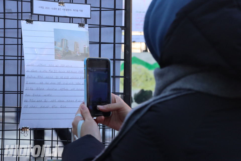 ‘여성홈리스가 나눈 집 이야기’ 전시 중 여성홈리스 당사자 사계절(가명) 씨의 ‘소중한 물건 사용설명서’를 한 시민이 휴대폰 카메라로 찍고 있다. 작품에는 무지개가 펼쳐진 서울역 전경을 직접 찍어 프린트한 사진과 글이 담겨 있다. 사진 복건우