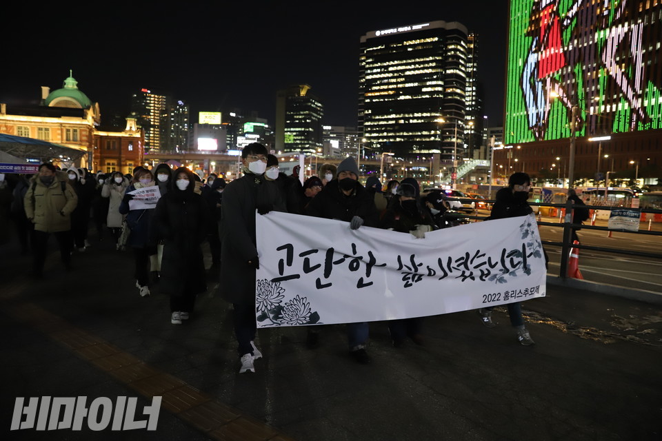 2022홈리스추모제공동기획단이 서울역 광장에서 대합실 쪽으로 행진하고 있다. 현수막에 “고단한 삶이셨습니다”라고 적혀 있다. 사진 하민지
