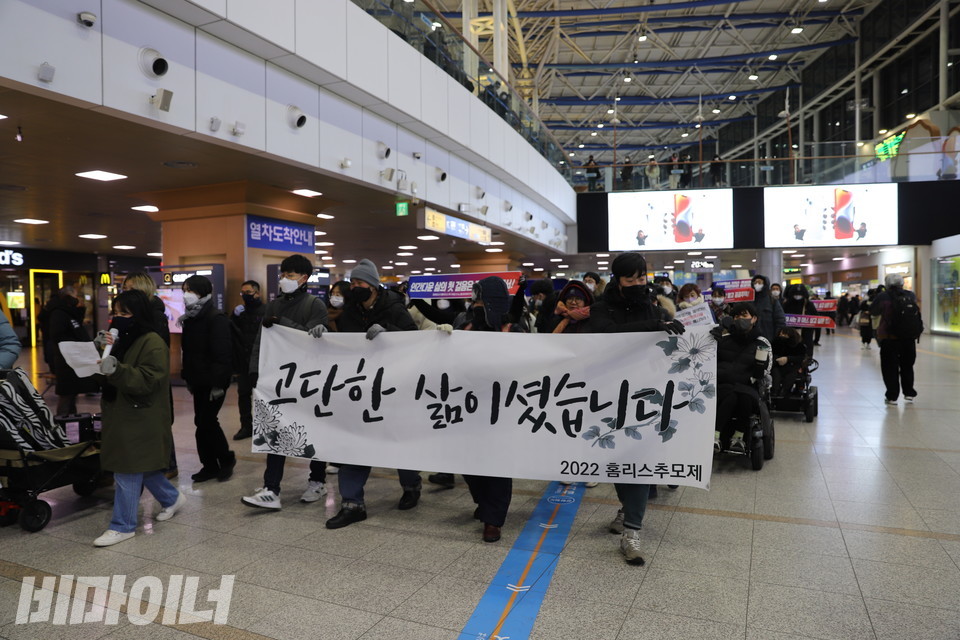 2022홈리스추모제공동기획단이 서울역 대합실 안에서 행진하고 있다. 현수막에 “고단한 삶이셨습니다”라고 적혀 있다. 사진 하민지