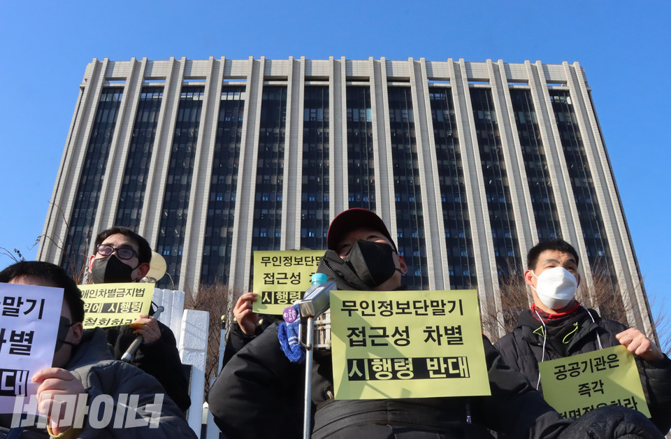 장애인차별금지추진연대 활동가들이 정부서울청사 앞에서 ‘무인정보단말기(키오스크) 접근성 차별 시행령 반대’라고 적힌 노란 손피켓을 들어 보이고 있다. 사진 복건우