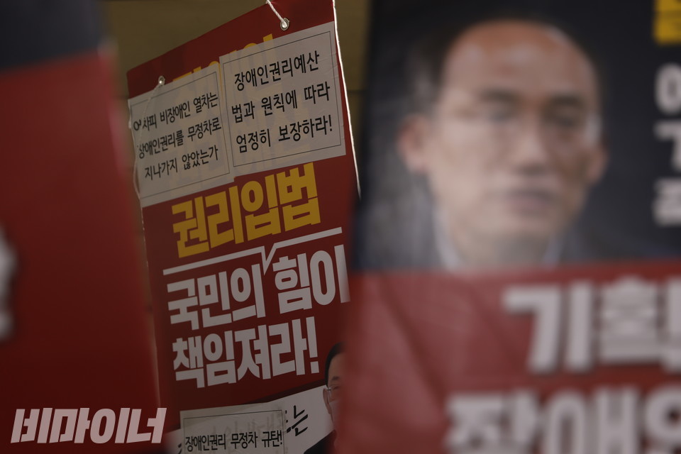 비장애인 활동가들이 들고 있던 피켓. 오른쪽에 추경호 기획재정부 장관 얼굴이 희미하게 보인다. 가운데에 “어차피 비장애인 열차는 장애인권리를 무정차로 지나지 않았는가. 장애인권리예산 법과 원칙에 따라 엄정히 보장하라! 권리입법, 국민의힘이 책임져라!”라고 적힌 피켓이 있다. 사진 하민지