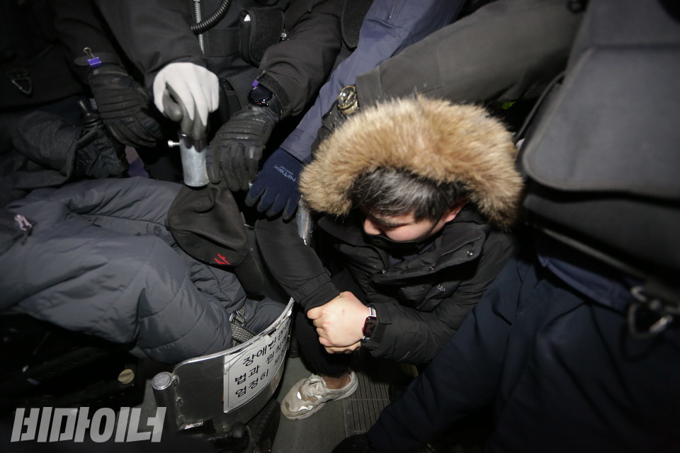 이규식 서울장애인차별철폐연대 대표의 하차를 막으며 서울교통공사 직원들이 휠체어를 뒤에서 잡아당기자, 한 비장애인 활동가가 이에 저항하며 휠체어 앞부분을 붙잡고 있다. 사진 강혜민