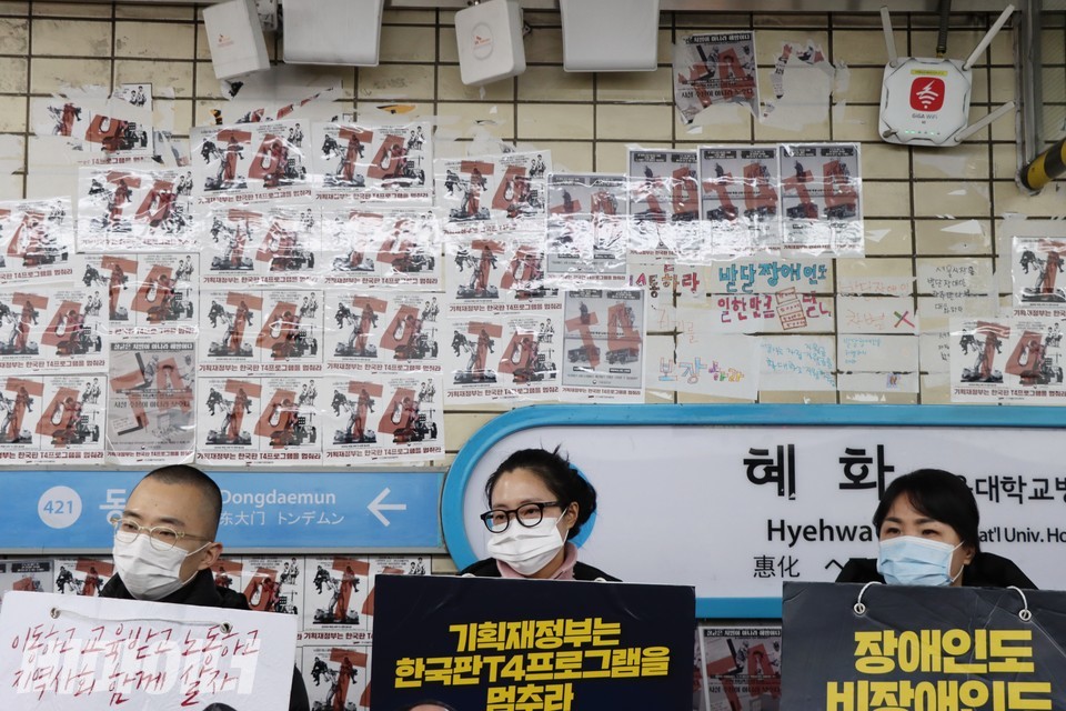 선전전에 참석한 시민들이 피켓을 들고 있다. 승강장 벽에는 “T4”라고 적힌 스티커가 빼곡히 붙어 있다. 사진 하민지