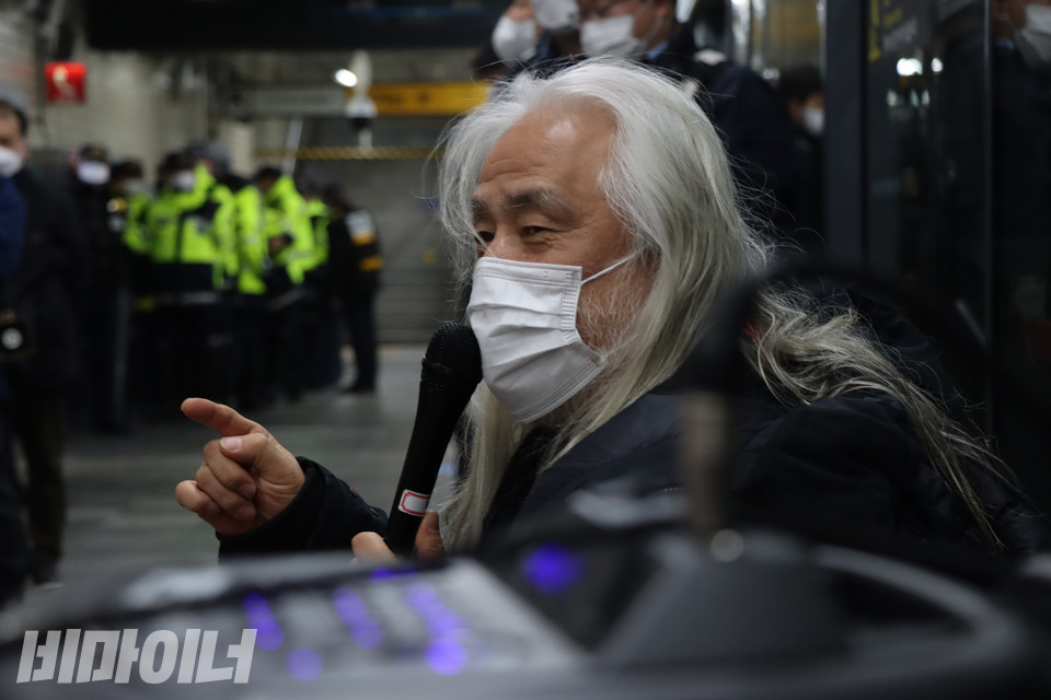 보라색 불빛이 들어오는 앰프 너머로 박경석 전국장애인차별철폐연대 상임공동대표가 마이크를 들고 발언하고 있다. 경찰과 서울교통공사 보안관이 멀찍이서 선전전을 지켜보고 있다. 사진 복건우