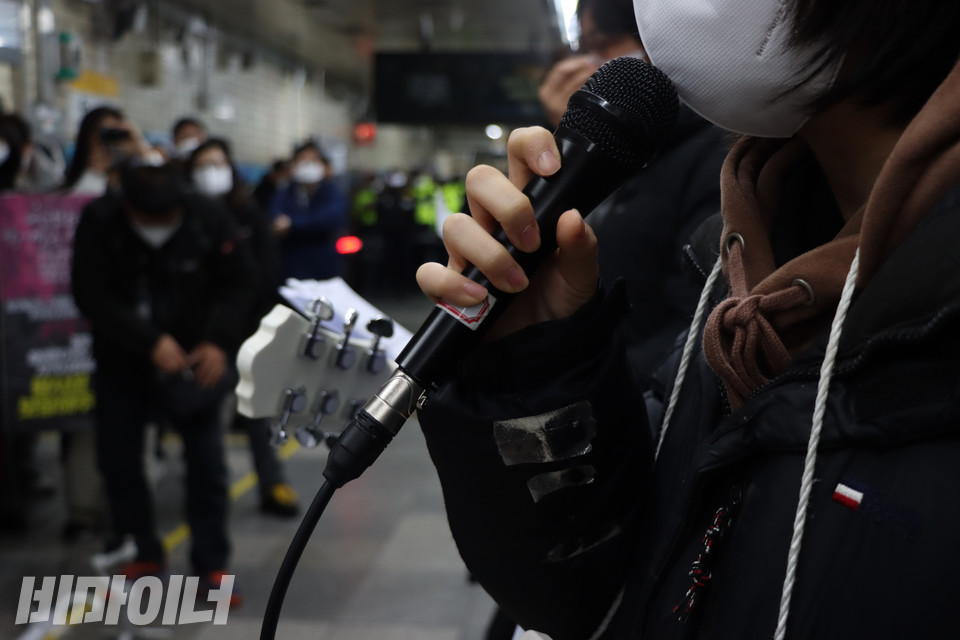 장애, 노동, 청소년 등 다양한 의제에서 목소리를 내는 활동가들로 결성된 ‘더딘밴드’가 선전전 시작을 알리는 공연을 펼치고 있다. 마이크를 든 피아 청소년인권활동가 뒤로 흰색 통기타와 악보지가 보인다. 사진 복건우