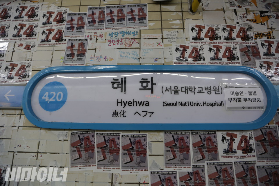 혜화역 승강장(동대문역사문화공원역 방향) 5-4. 벽면에 있는 혜화역 표지판에는 “서울교통공사. 미승인·불법 부착물 부착금지”라는 안내문이 붙어 있다. 그 주변 벽면에는 비용을 이유로 장애인권리예산을 보장하지 않는 기획재정부를 규탄하는 전장연 T4선전물이 있다. 사진 강혜민