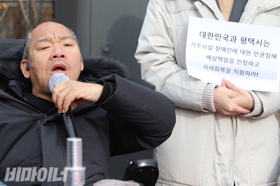 이규식 서울장애인차별철폐연대 공동대표가 발언 중이다. 그의 옆에는 “대한민국과 평택시는 거주시설 장애인에 대한 인권침해 배상책임을 인정하고 피해회복을 지원하라!”라고 적힌 손팻말이 보인다. 사진 하민지