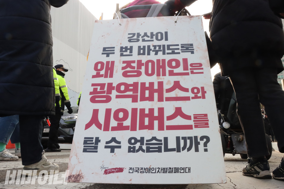 한 장애인 활동가의 휠체어 뒤편에 검은색과 붉은색으로 ‘강산이 두 번 바뀌도록 왜 장애인은 광역버스와 시외버스를 탈 수 없습니까’라고 적힌 피켓이 걸려 있다. 사진 복건우