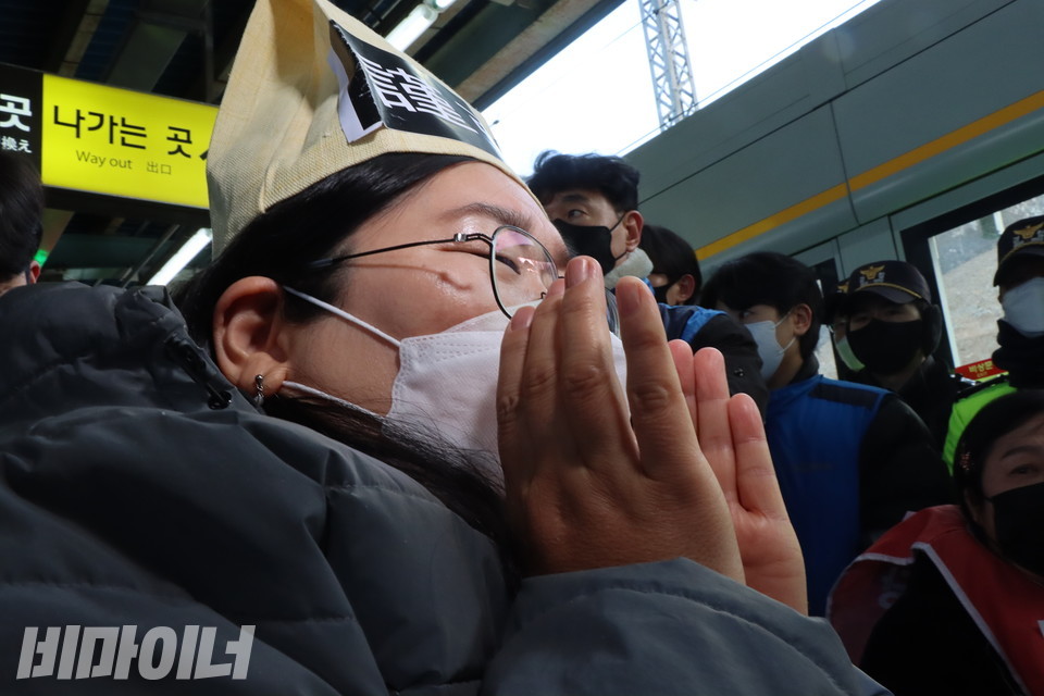 한자로 ‘근조’라고 적힌 두건(頭巾, 장례 모자)을 쓴 김선영 나무를심는장애인야학 교장이 두 손을 모아 “장애인도 열차에 타게 해주십시오”라고 외치고 있다. 사진 복건우권달주 대표는 '근조'라고 적힌 두건(頭巾, 장례 모자)