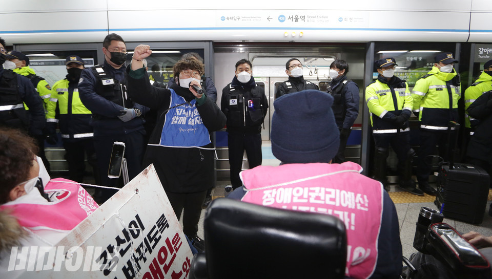 열차가 왔지만 서울교통공사 보안관이 출입구를 가로막고 있어 탑승할 수 없다. 한산한 열차 내부가 보인다. 성가연 전장연 활동가가 정리집회를 하며 구호를 외치고 있다. 사진 강혜민