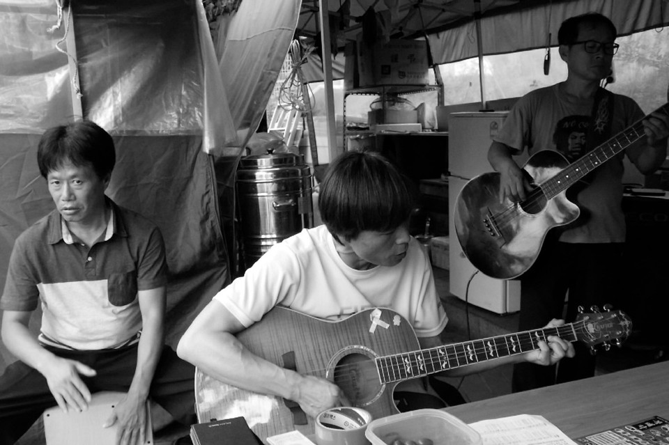 농성장에서 기타를 치는 콜트·콜텍 해고노동자들. 제일 왼쪽에서 카혼을 치는 사람이 임재춘. 사진 시네마달