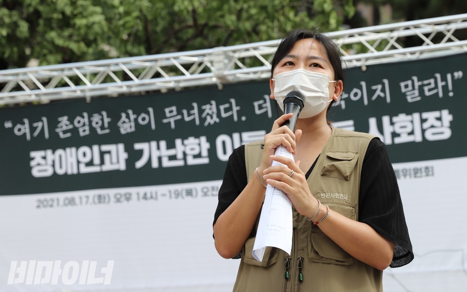 2021년 8월 17일, 복지 사각지대에서 죽어간 장애인과 가난한 이들을 추모하는 합동 사회장이 열렸다. 사회를 보고 있는 김윤영 빈곤사회연대 활동가. 그의 뒤로 ‘여기 존엄한 삶이 무너졌다. 더 이상 죽이지 말라!’라고 적힌 문구가 보인다. 사진 하민지