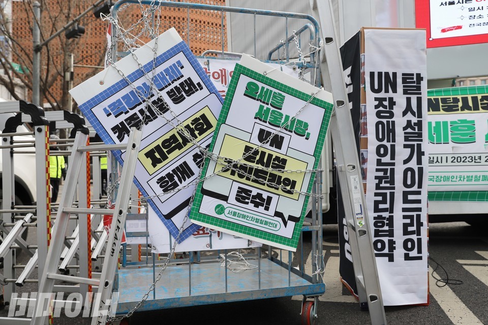 고발대회 현장에 있던 설치물. 철장에 오세훈 서울시장을 규탄하는 내용의 피켓이 걸려 있고 그 위에 쇠사슬이 묶였다. 옆에는 종이상자 여러 개가 쌓여 있는데, 그 위에 유엔장애인권리협약과 탈시설 가이드라인이 적힌 현수막이 붙어 있다. 사진 하민지