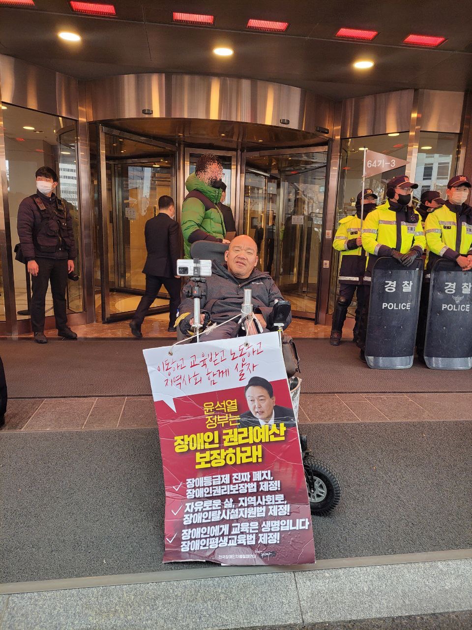 이규식 서울장애인차별철폐연대 상임대표가 웨스틴조선서울호텔 앞에서 1인 피케팅 중이다. 경찰들이 호텔 문 앞을 가로막고 있다. 사진 박온슬 나야장애인인권교육센터 활동가