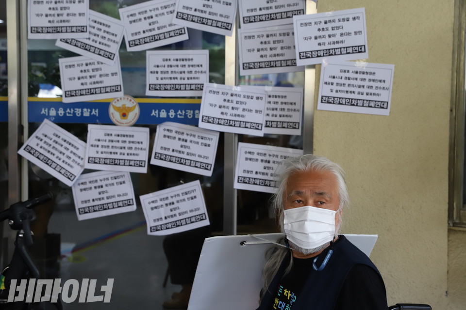 지난해 7월 19일, 박경석 전장연 상임공동대표가 용산서 정문 앞에 있다. 정문에는 장애인편의시설을 제공하지 않은 용산서를 규탄하는 피켓들이 붙어 있다. 사진 하민지