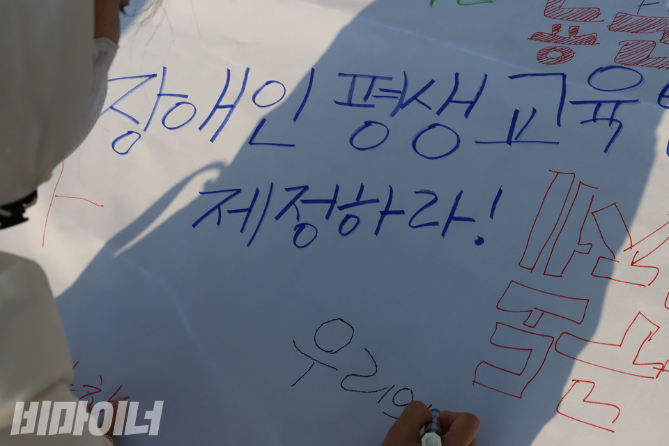 23일 오전 국회 앞 기자회견에 나선 장애인야학 학생이 흰 천 위에 장애인평생교육법 제정을 촉구하는 문구를 쓰는 퍼포먼스를 벌이고 있다. 사진 복건우