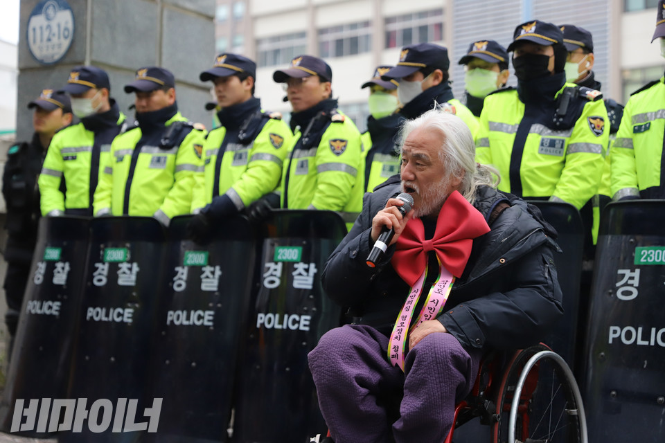 28일 오전 서울 종로구 혜화경찰서 입구에 방패를 든 경찰력에 둘러싸인 박경석 전국장애인차별철폐연대 상임공동대표가 목에 빨간 리본을 걸고 발언하고 있다. 사진 복건우
