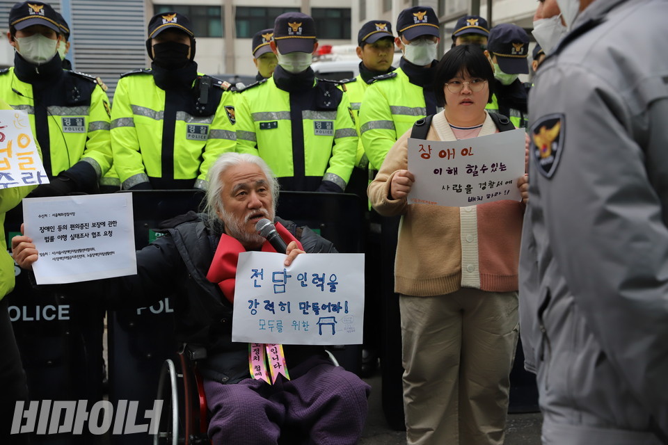 28일 오전 서울 종로구 혜화경찰서 입구에 방패를 든 경찰력에 둘러싸인 박경석 전국장애인차별철폐연대 상임공동대표(왼쪽)가 서울 시내 31개 경찰서 내 장애인 편의증진 실태조사 협조를 요청하는 공문을 들어 보이며 경찰을 향해 발언하고 있다. 사진 복건우
