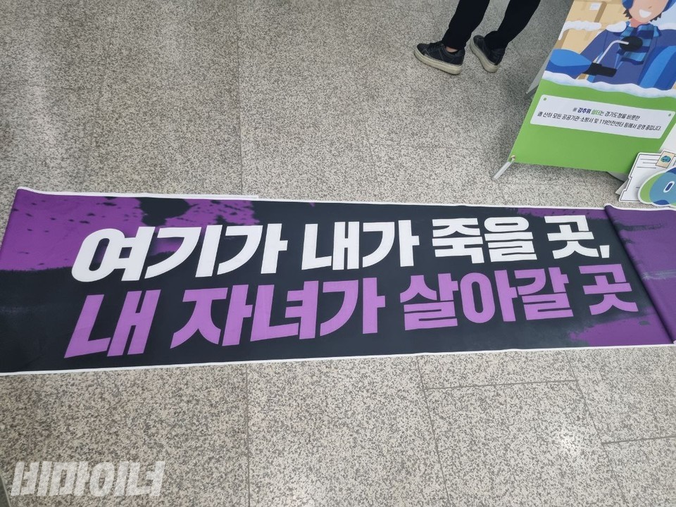 경기도청 로비 바닥에 현수막이 펼쳐져 있다. “여기가 내가 죽을 곳, 내 자녀가 살아갈 곳”이라고 적혀 있다. 사진 박정수