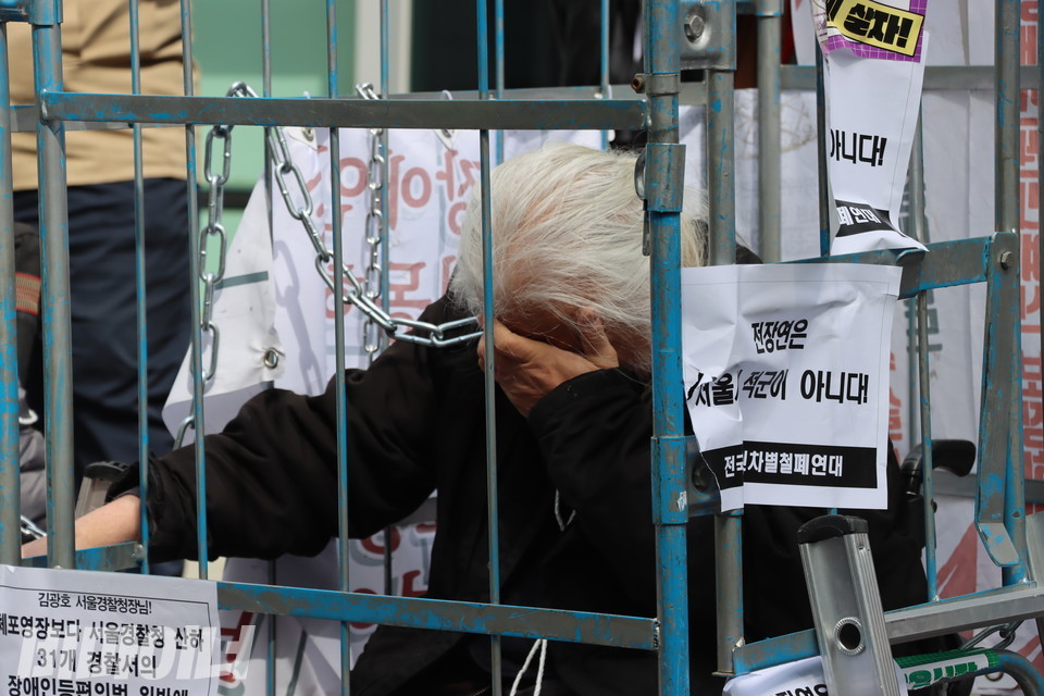 박경석 전장연 상임공동대표가 마른세수를 하고 있다. 그의 목에 감긴 쇠사슬은 철창 밖 다른 장애인 활동가와 연결돼 있다. 사진 하민지