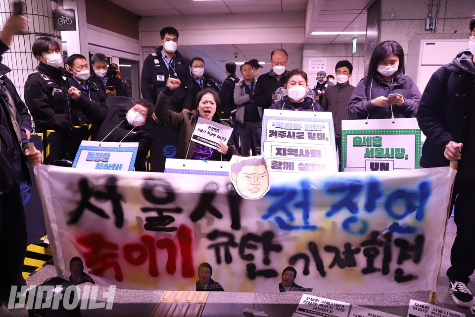 21일 오전 8시, 전장연 활동가들이 1호선 시청역(청량리 방면) 승강장 10-4에서 기자회견을 하고 있다. 현수막에는 ‘서울시 전장연 죽이기 규탄 기자회견’ 글자가 세 가지 스프레이를 이용해 알록달록 쓰여 있으며, 위쪽엔 오세훈 서울시장 캐리커처가 붙어 있다. 사진 강혜민 