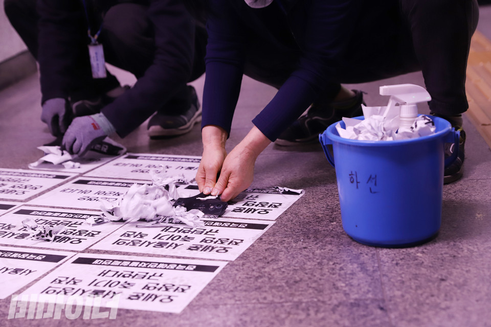 바닥에 붙어 있는 장애인 권리보장 촉구 스티커를 환경미화원과 서울교통공사 직원이 떼어내고 있다. 사진 강혜민