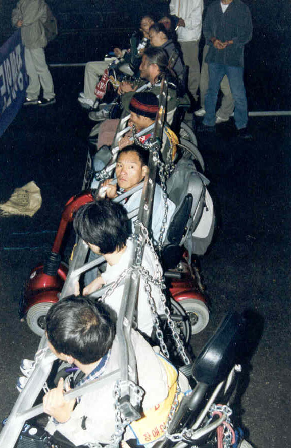 2001년 10월 31일, 종로에서 장애인들이 버스를 막아 세우고 있다. 경찰 진압에 대비해 이들은 사다리와 쇠사슬로 서로를 묶었다. 이규식이 옆을 돌아보고 있다. 사진 장애인이동권연대 