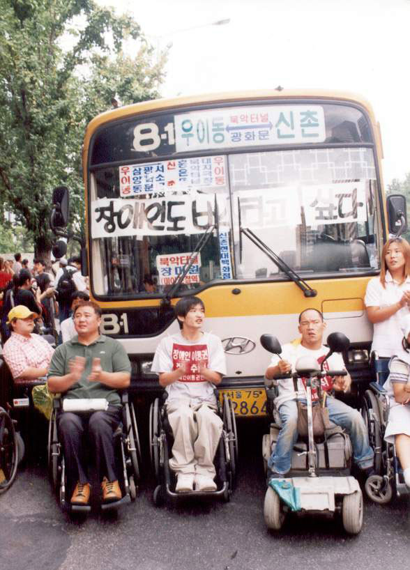 2001년 9월, 8-1번 버스를 막아 세운 장애인들. 버스 앞면에는 “장애인도 버스 타고 싶다”는 피켓이 붙어 있다. 사진 오른쪽에 스쿠터를 탄 이규식이 있다. 사진 장애인이동권연대  