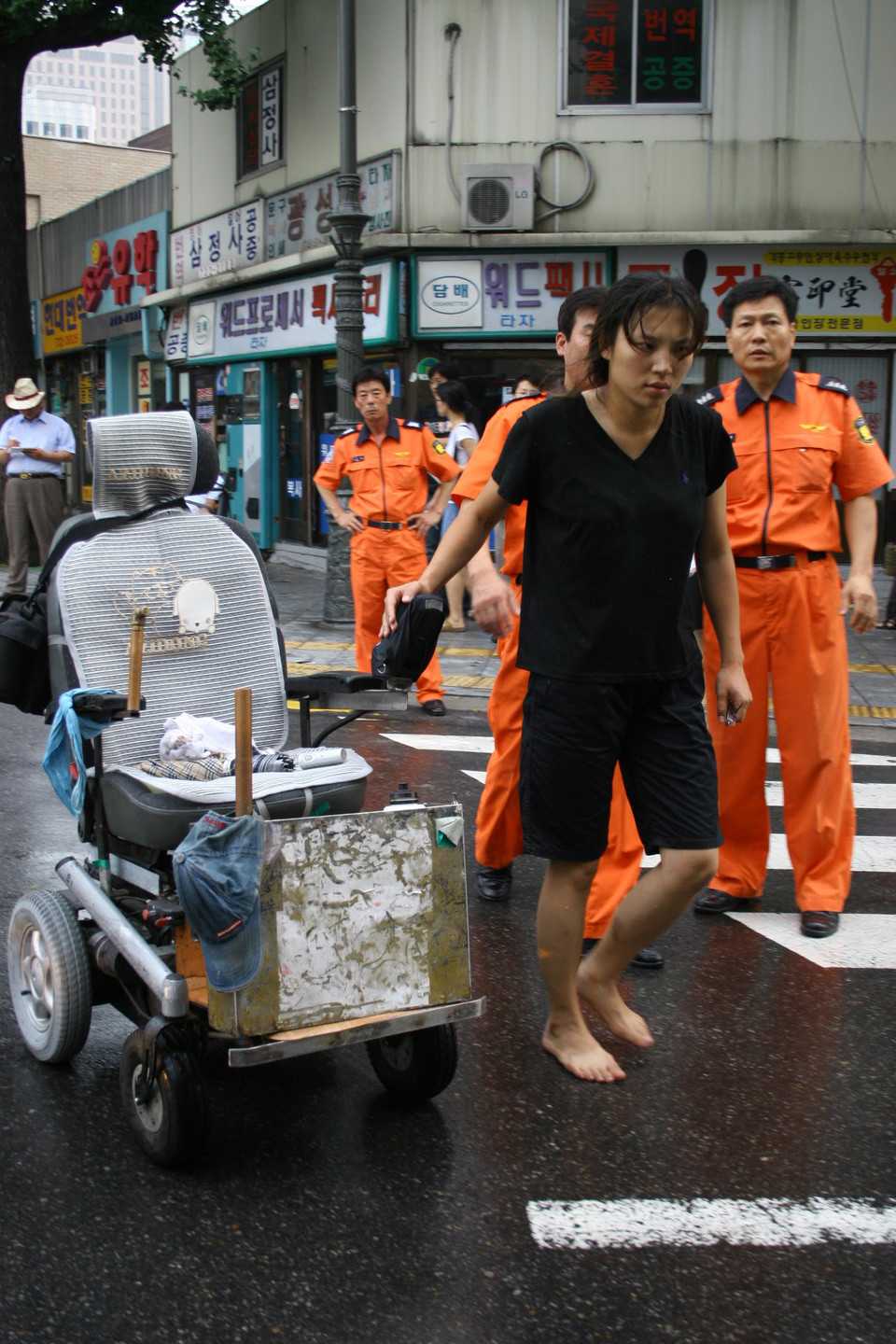 2006년 8월 7일, 종로구청이 S재단 비리 해결을 촉구하는 농성장을 침탈하고 부쉈다. 그 과정에서 저항하던 이규식의 휠체어가 옆으로 넘어졌고, 그의 목을 종로구청 직원이 밟고 지나갔다. 결국 이날 이규식은 응급실에 실려 갔다. 김정하 발바닥행동 활동가가 텅 빈 그의 휠체어를 일으켜 옮기고 있다. 몸싸움하느라 신발이 날아가 맨발이다. 사진 전진호 