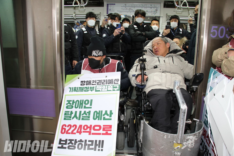 2021년 12월 31일, 여의도역에서 이규식이 지하철 문을 막아서고 있다. 그 뒤로 검은 옷을 입은 서울교통공사 지하철 보안관들이 핸드폰으로 촬영을 하거나 팔짱을 낀 채 이를 바라보고 있다. 사진 강혜민