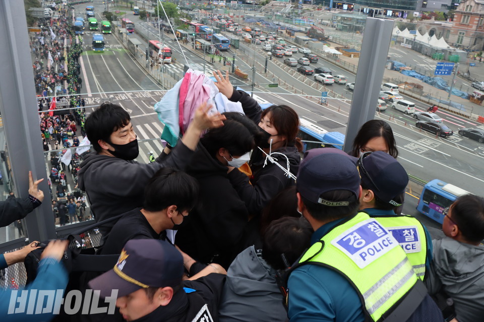 서울로7017에서 대형 현수막을 내리려다가 경찰들에게 현수막을 빼앗기고 폭력적으로 진압 당하는 활동가들. 이 현장에서 두 명이 연행됐다. 이들 뒤로 행진하는 사람들의 모습이 보인다. 사진 복건우 