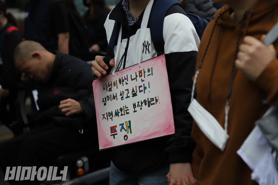 행진하는 사람들. 목에 걸린 피켓에는 ‘시설이 아닌 나만의 집에서 살고 싶다! 지역사회는 보장하라! 투쟁’이라고 적혀 있다. 사진 강혜민