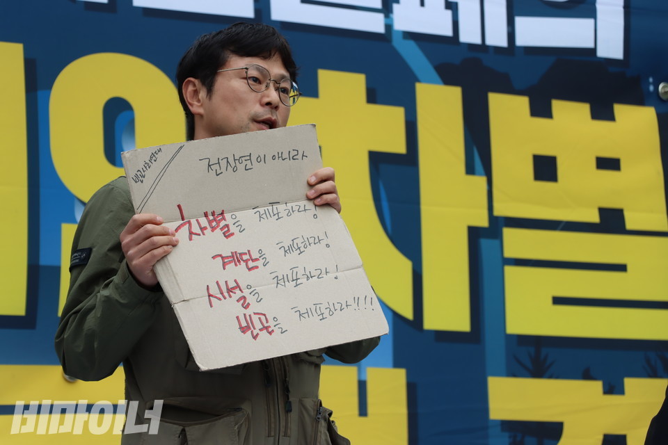 이원호 빈곤사회연대 집행위원장이 발언하고 있다. 그의 손에는 “차별을 체포하라! 계단을 체포하라! 시설을 체포하라! 빈곤을 체포하라!”고 적힌 피켓이 들려 있다. 피켓은 상자를 잘라서 만들었다. 사진 강혜민