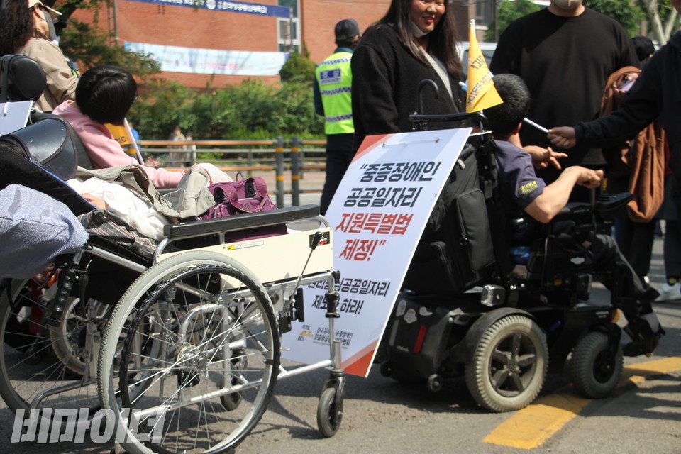 두 명의 휠체어 탄 장애인 사이로 “중증장애인 공공일자리 지원특별법 제정하라!”고 적힌 피켓이 있다. 사진 강혜민  