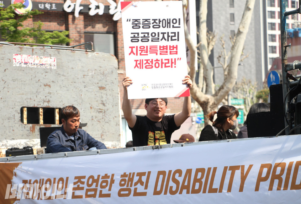 트럭 위에서 한 남성이 “중증장애인 공공일자리 지원특별법 제정하라!”고 적힌 피켓을 번쩍 들어 보이고 있다. 사진 강혜민