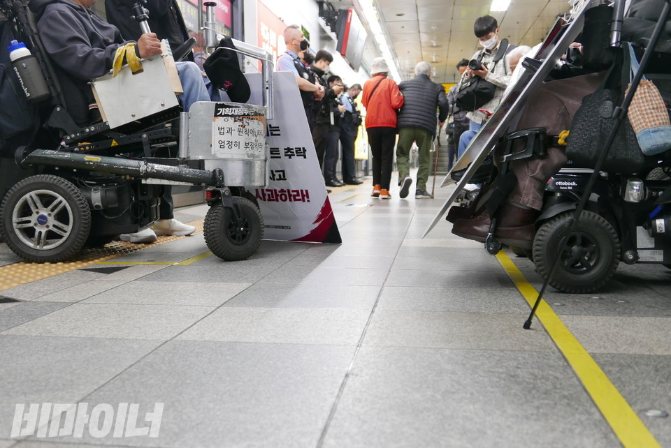 양쪽에 휠체어 이용자가 있다. 가운데에 노인이 지나가고 있다. 사진 양유진